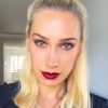 Love London: A person with long blonde hair in a top knot poses indoors, showcasing a Swedish look. They are wearing bold red lipstick and dark eye makeup, exuding elegance with their neutral expression. The softly lit room in the background sets the perfect stage for a chic makeup tutorial.