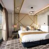 Love London: A luxurious Southend hotel room features a large bed, elegant gold and white decor, and a geometric patterned carpet. A large window showcases a scenic ocean view—a perfect reason to visit. A modern hanging light fixture and adjacent bathroom add to the opulent atmosphere.