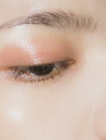 Love London: Close-up of a closed eye with dewy, soft pink eyeshadow applied above the eyelid, showcasing a well-groomed eyebrow and glowing, radiant skin.