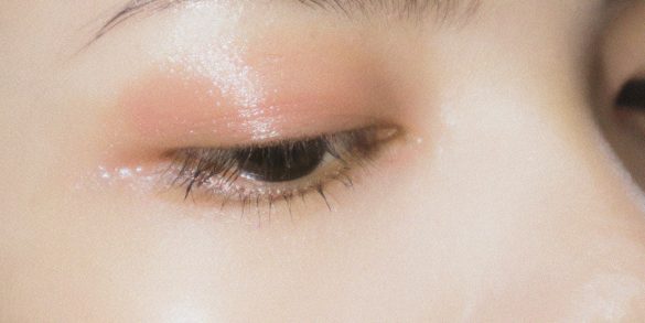 Love London: Close-up of a closed eye with dewy, soft pink eyeshadow applied above the eyelid, showcasing a well-groomed eyebrow and glowing, radiant skin.