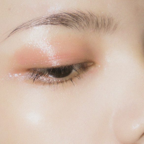 Love London: Close-up of a closed eye with dewy, soft pink eyeshadow applied above the eyelid, showcasing a well-groomed eyebrow and glowing, radiant skin.