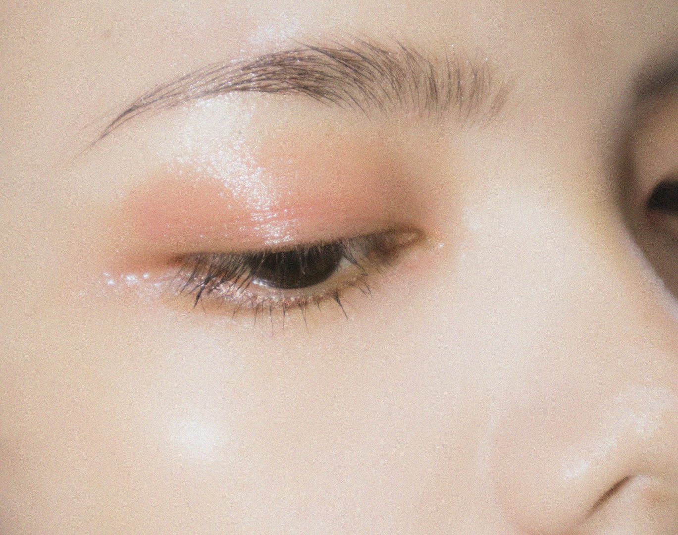 Love London: Close-up of a closed eye with dewy, soft pink eyeshadow applied above the eyelid, showcasing a well-groomed eyebrow and glowing, radiant skin.